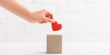 Papierherz wird von einer Hand in eine Box gelegt