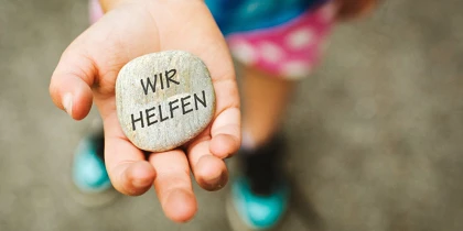 Kind hält einen Stein auf dem "WIR HELFEN" steht